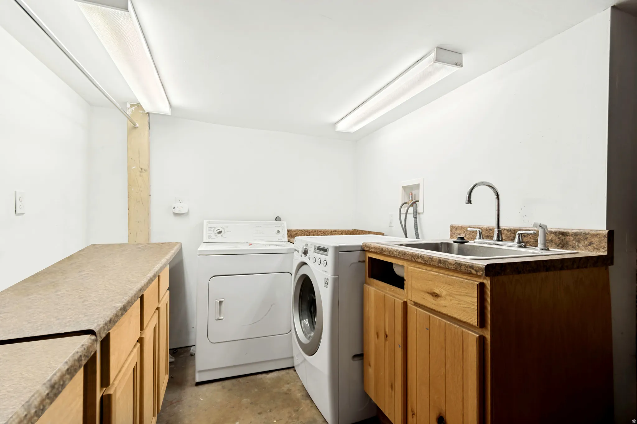 Dedicated laundry area featuring a utility sink, wood-finish cabinetry, extensive countertop space, and overhead fluorescent lighting