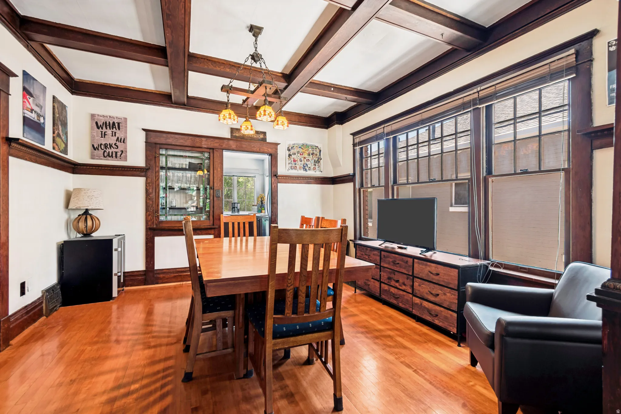 Hardwood flooring throughout, featuring a coffered ceiling with dark wood beams, extensive dark wood trim, and a built-in display cabinet with leaded glass panels