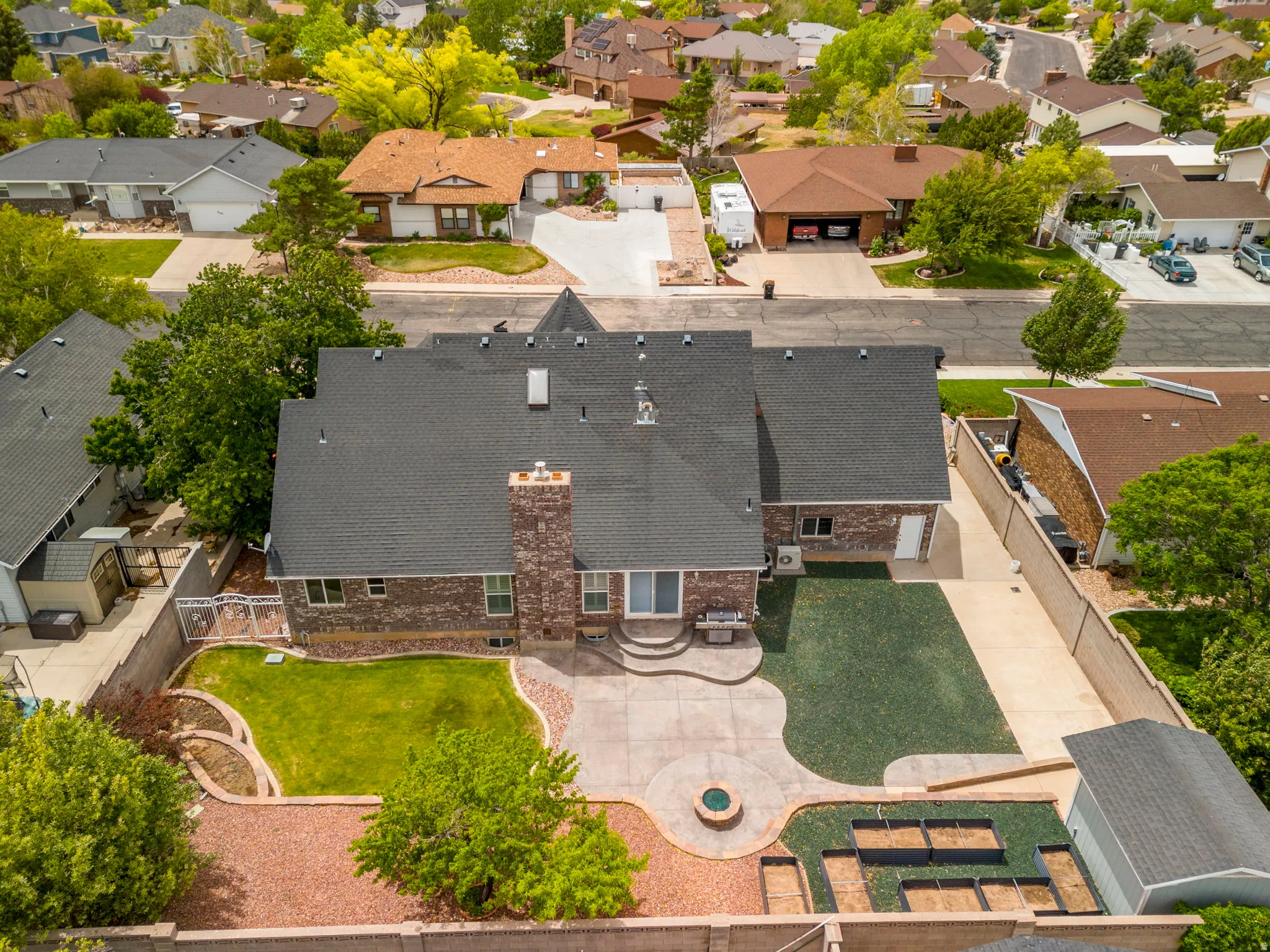Aerial property view featuring a dark shingle roof, a brick chimney, and a concrete patio with an integrated fire pit