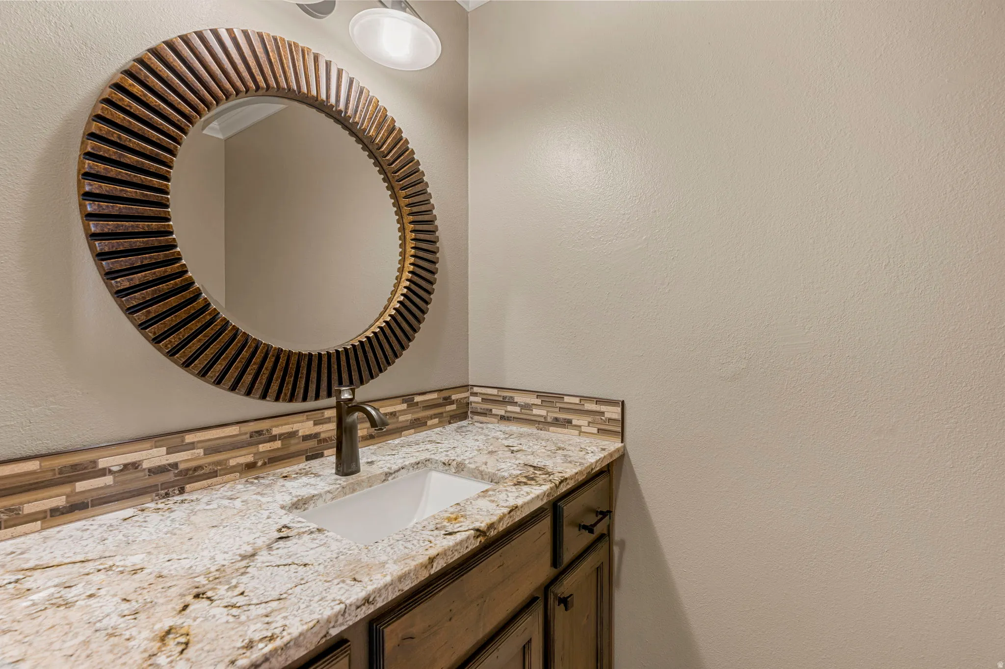 Bathroom vanity featuring a granite countertop with an undermount sink, a bronze-finish faucet, and a mosaic tile backsplash