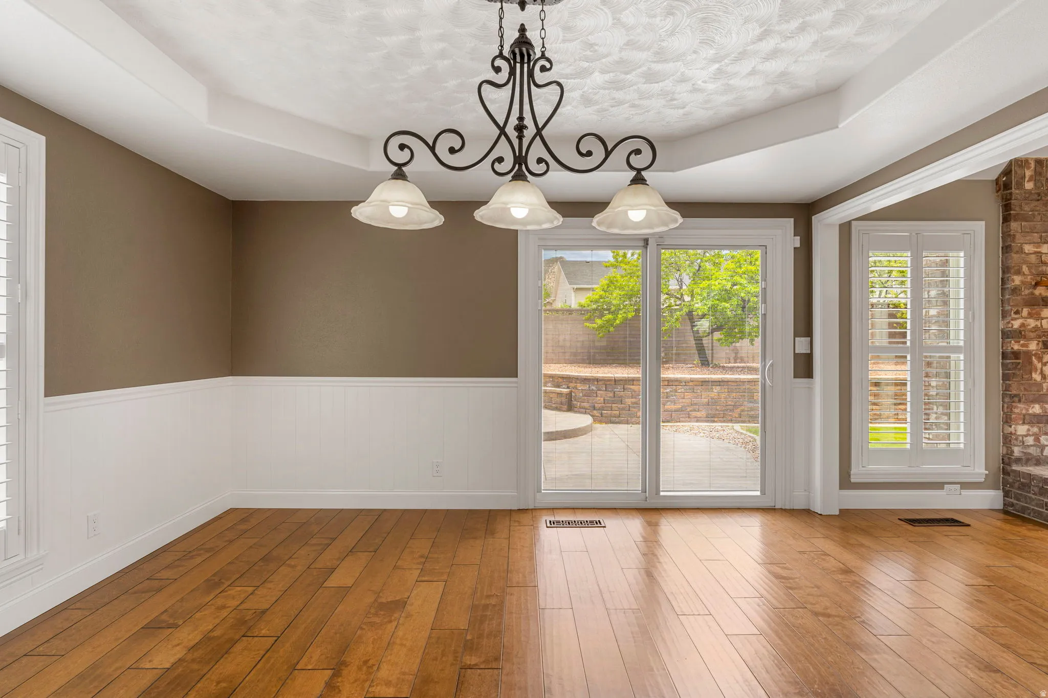 Bright interior space featuring wood-finish flooring, wainscoting, and a tray ceiling with a decorative chandelier