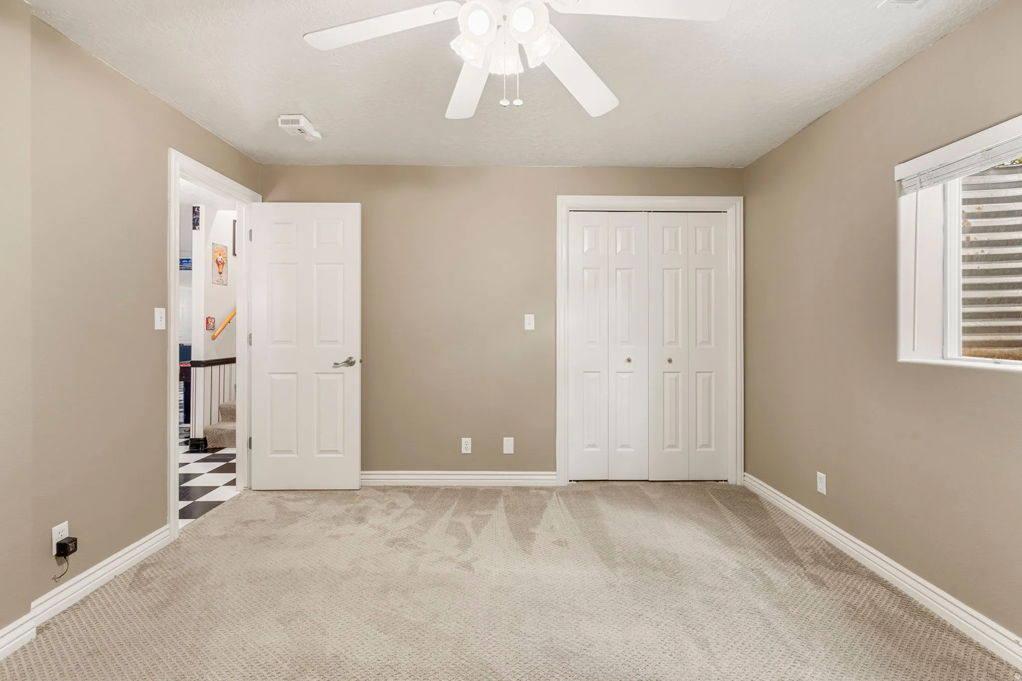 Neutral-toned wall paint throughout, plush carpeting, bi-fold closet doors, white trim, and a ceiling fan with integrated lighting