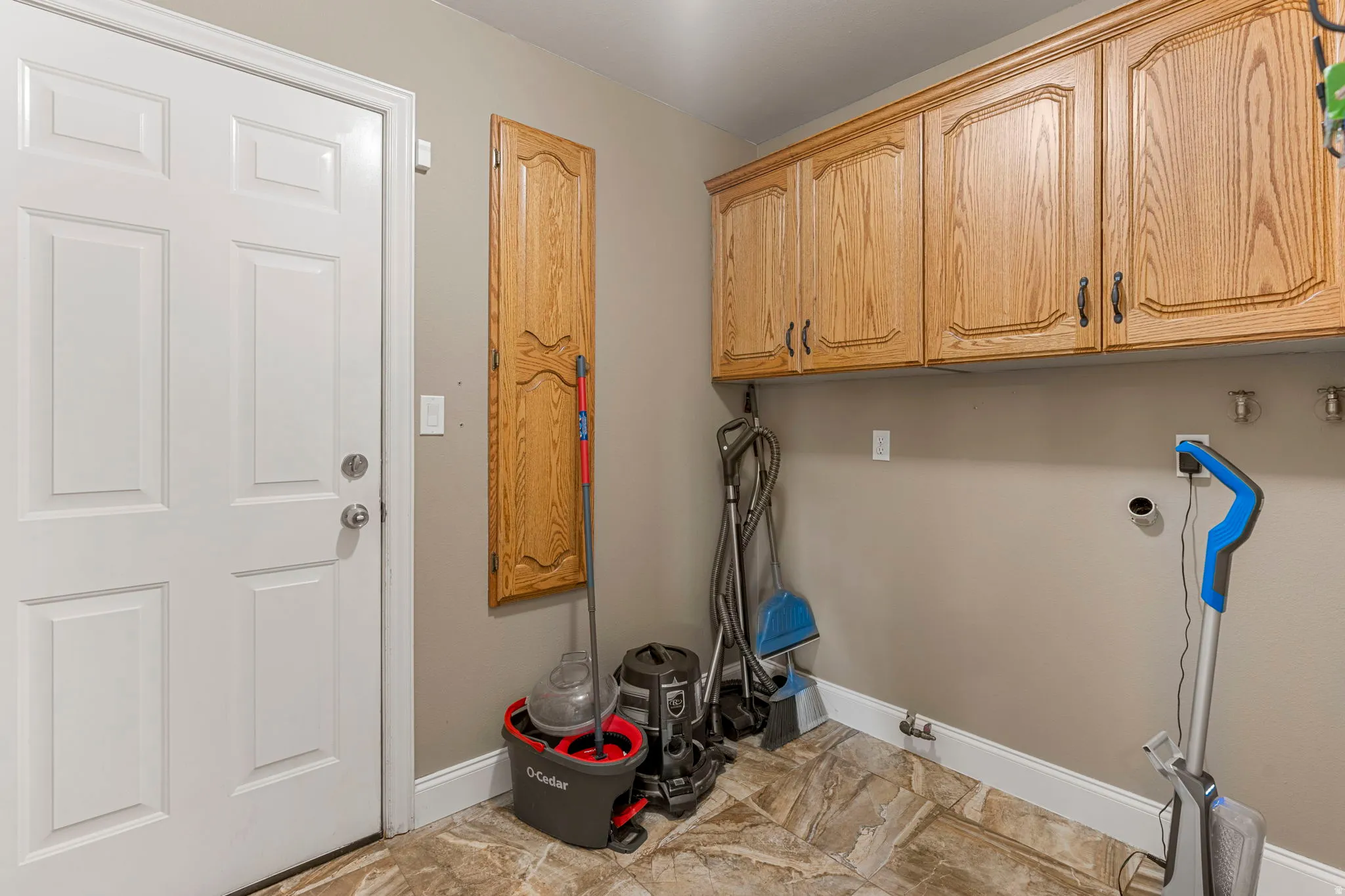 Utility room with wood-finish upper cabinetry, a dedicated storage cabinet, a white paneled door, and patterned tile flooring