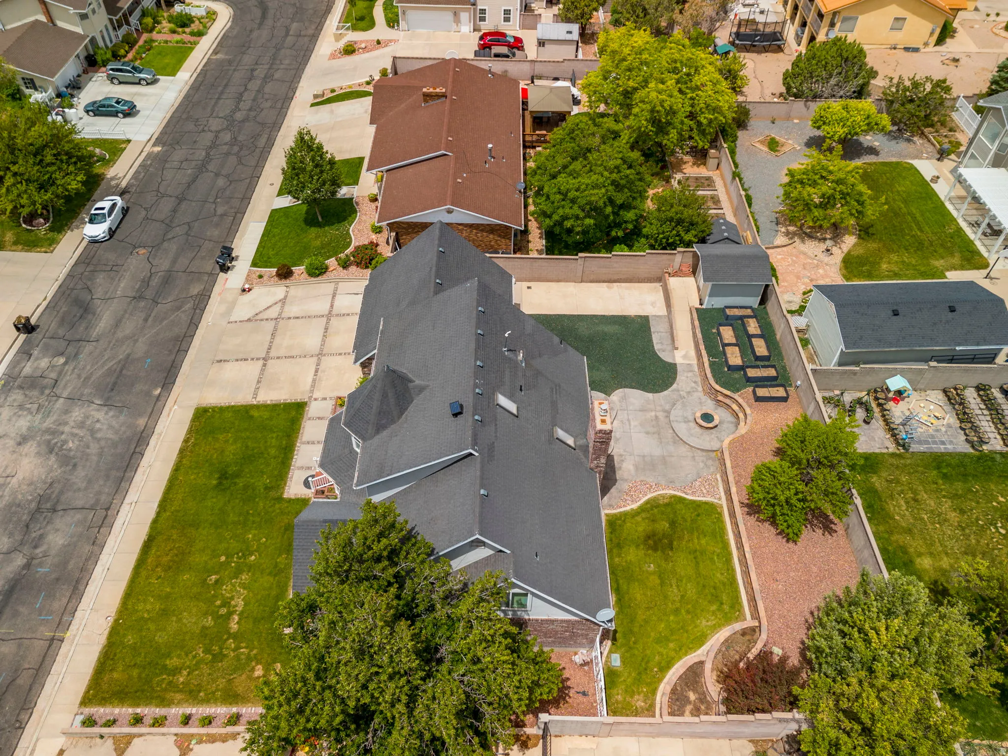 Expansive property featuring a multi-gabled roofline, varied landscaping with turf and hardscaping, a circular patio with a fire pit, and a storage shed