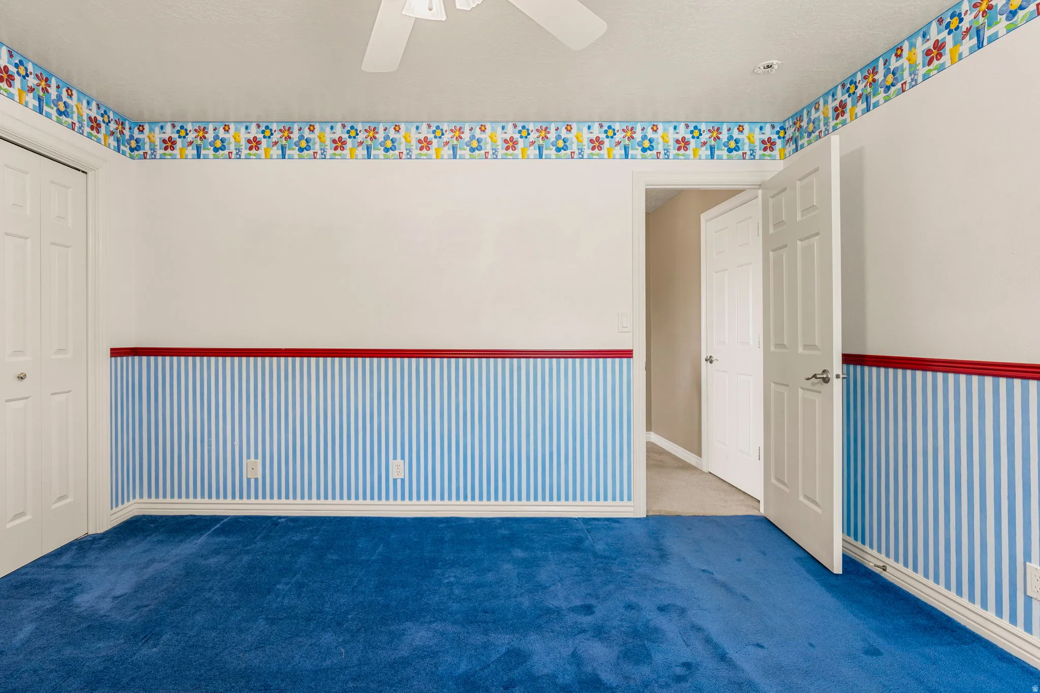 Room featuring blue carpet, white walls with blue and white striped wainscoting, and a decorative floral border