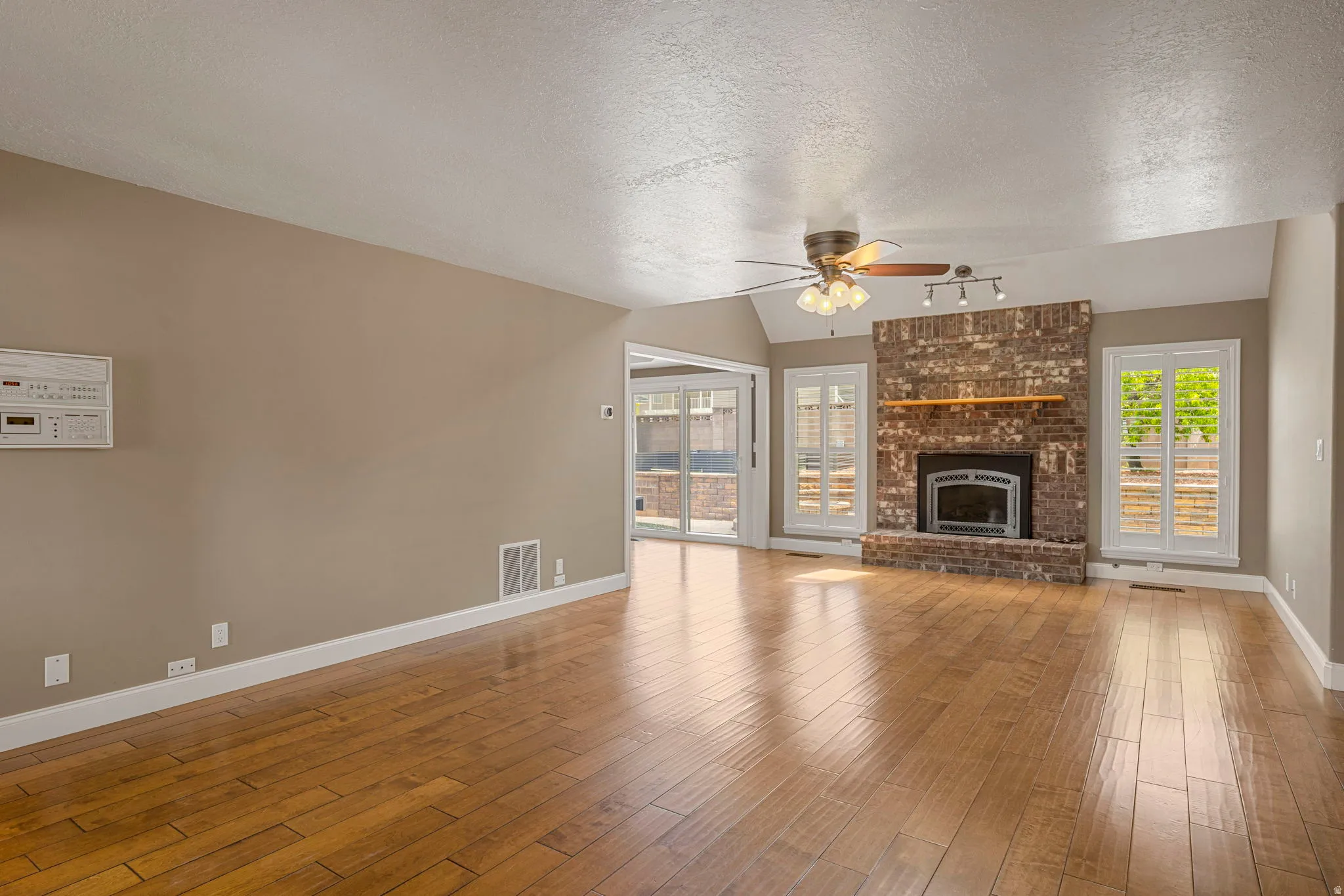 Spacious living area featuring wood-finish flooring, a vaulted ceiling, and a brick-faced fireplace with an integrated mantel