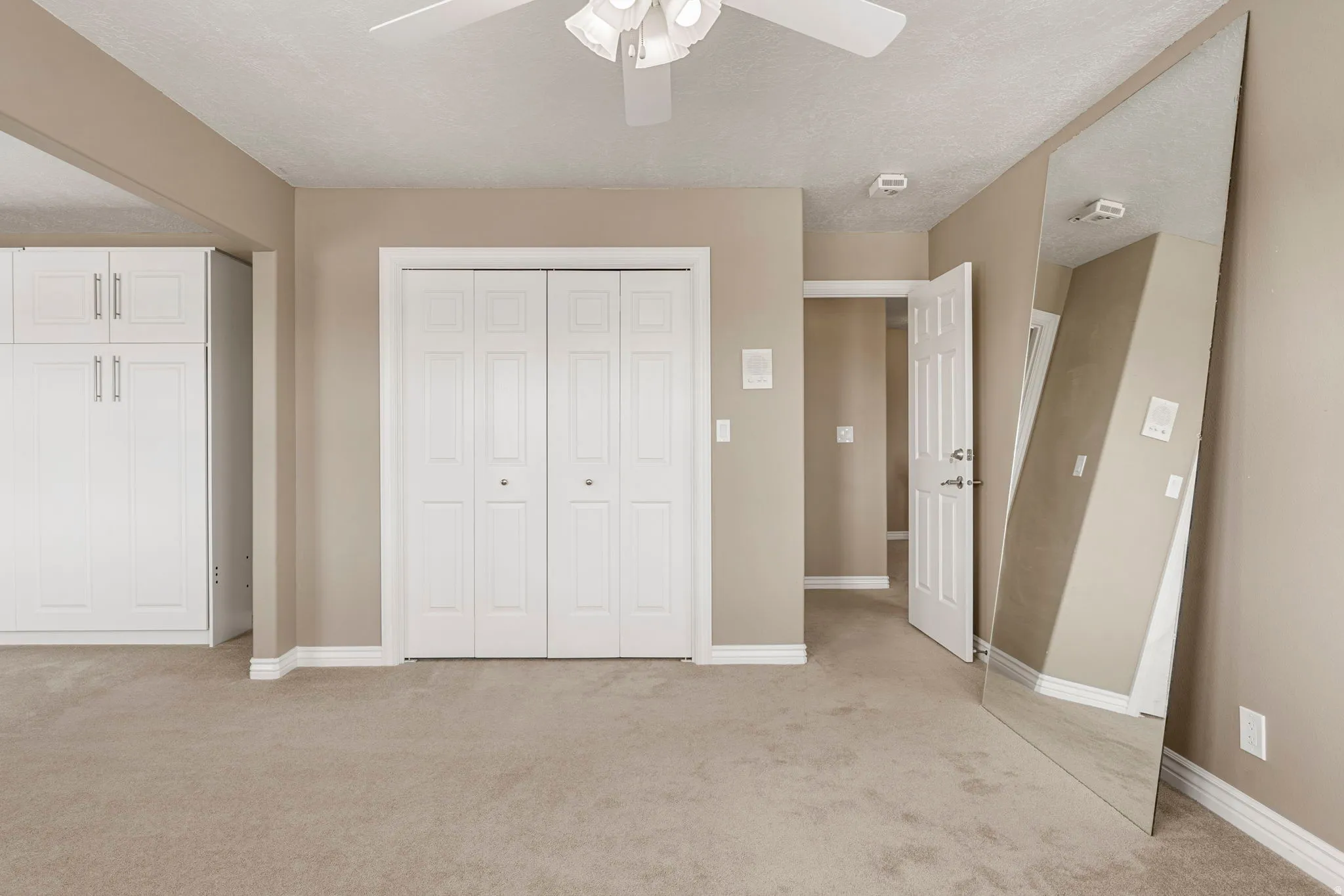 Neutral-toned room featuring light beige carpeting, white bi-fold closet doors, and white built-in cabinetry with silver-tone hardware