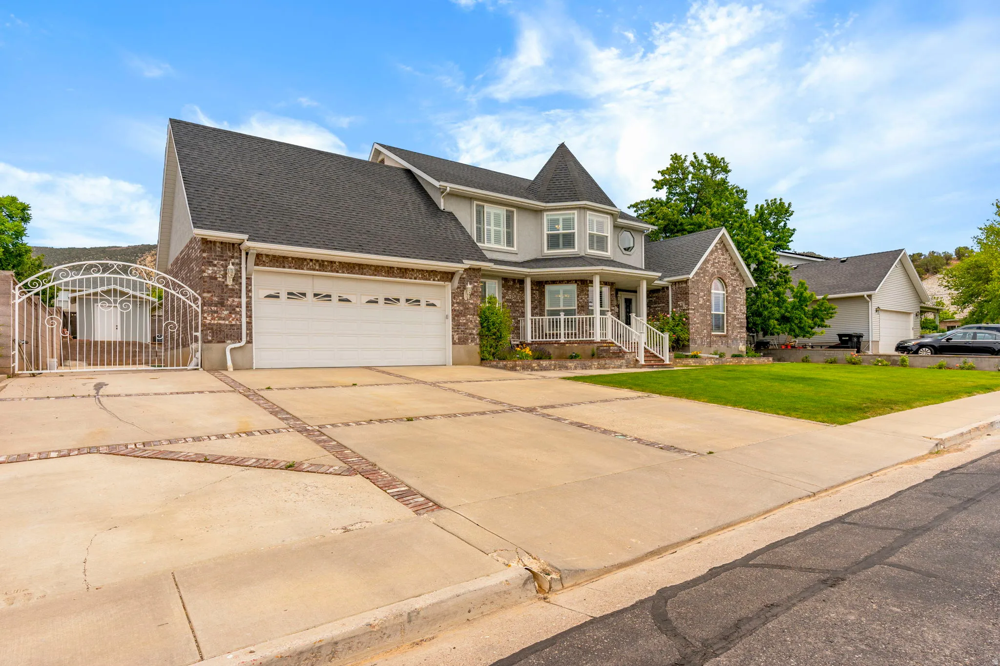 Two-story residence featuring a brick and siding exterior, an attached two-car garage, an ornate driveway gate, and a prominent front porch with white railing