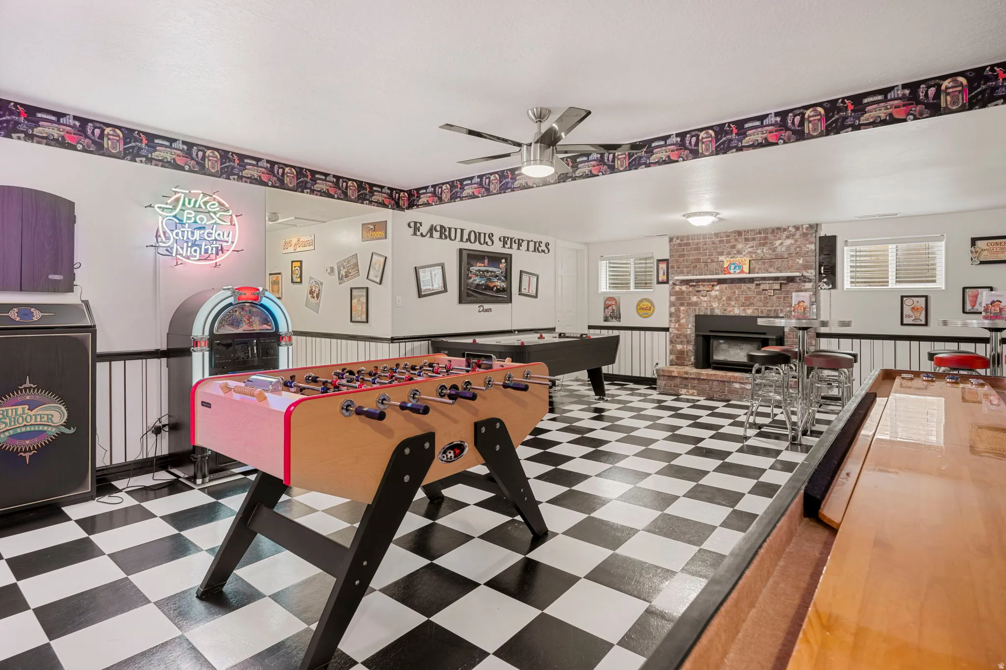 Spacious entertainment room featuring checkerboard flooring, a brick fireplace, white wainscoting, and recessed lighting