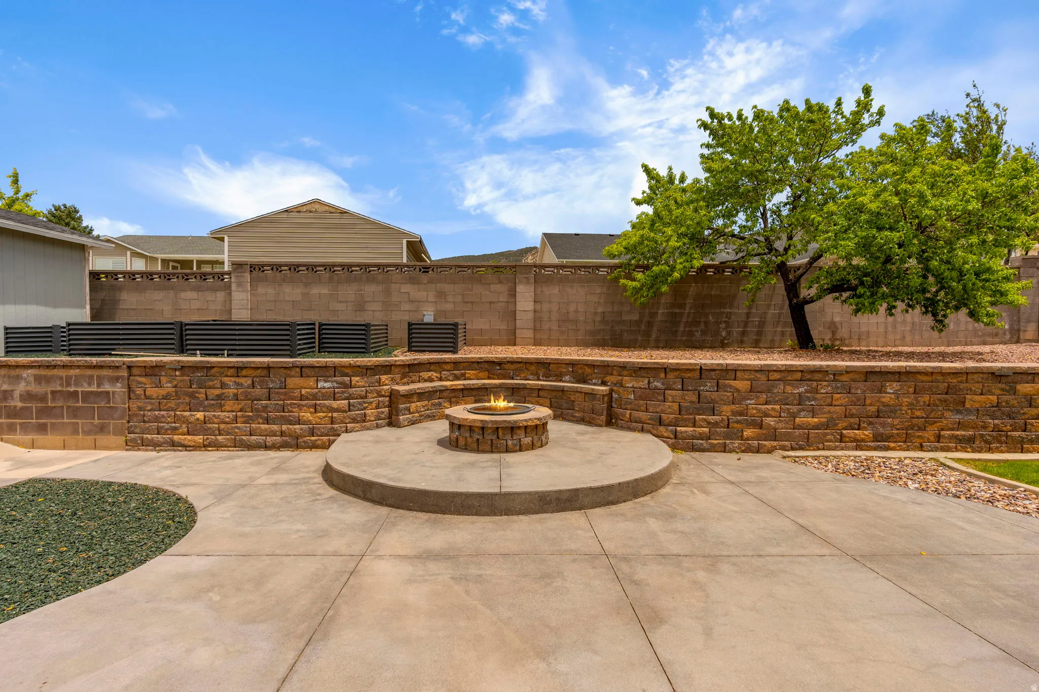 Expansive concrete patio featuring a built-in stone fire pit with integrated stone bench seating
