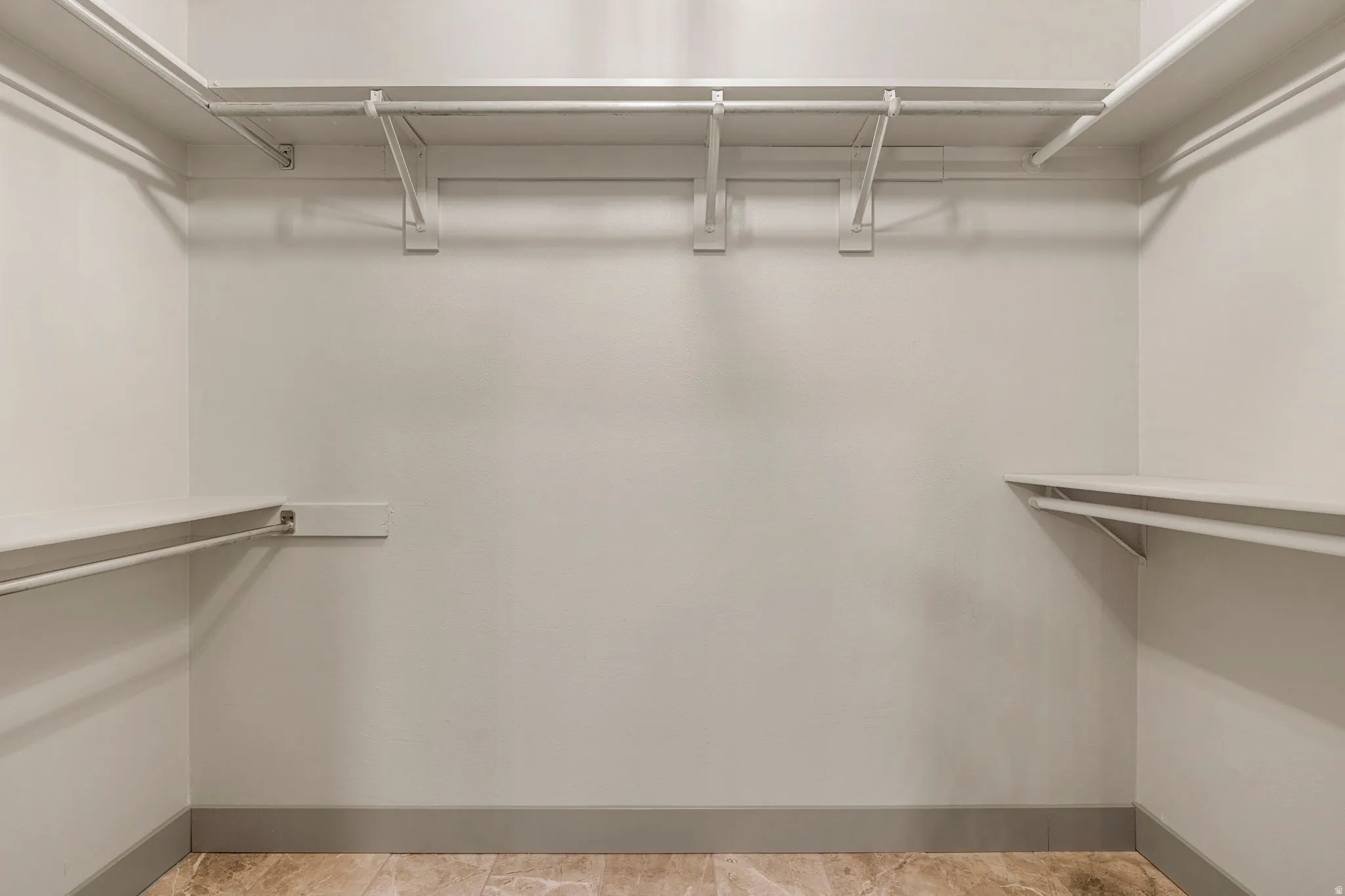 Spacious closet featuring multiple white wire shelving units, integrated hanging rods, light-toned wall paint, gray baseboards, and patterned floor tiling