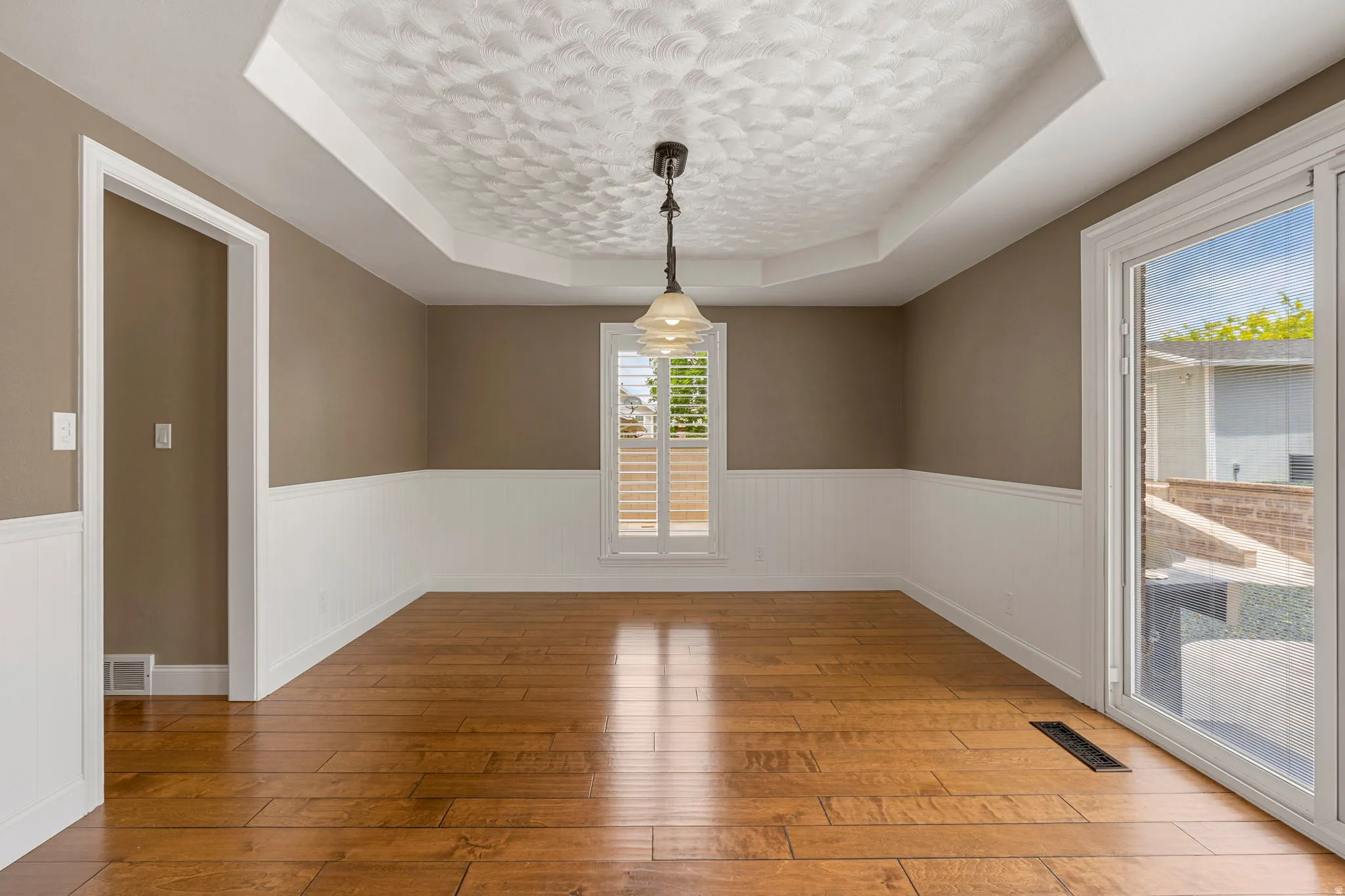 Spacious room featuring wood-finish flooring, white wainscoting, and a tray ceiling with a textured finish