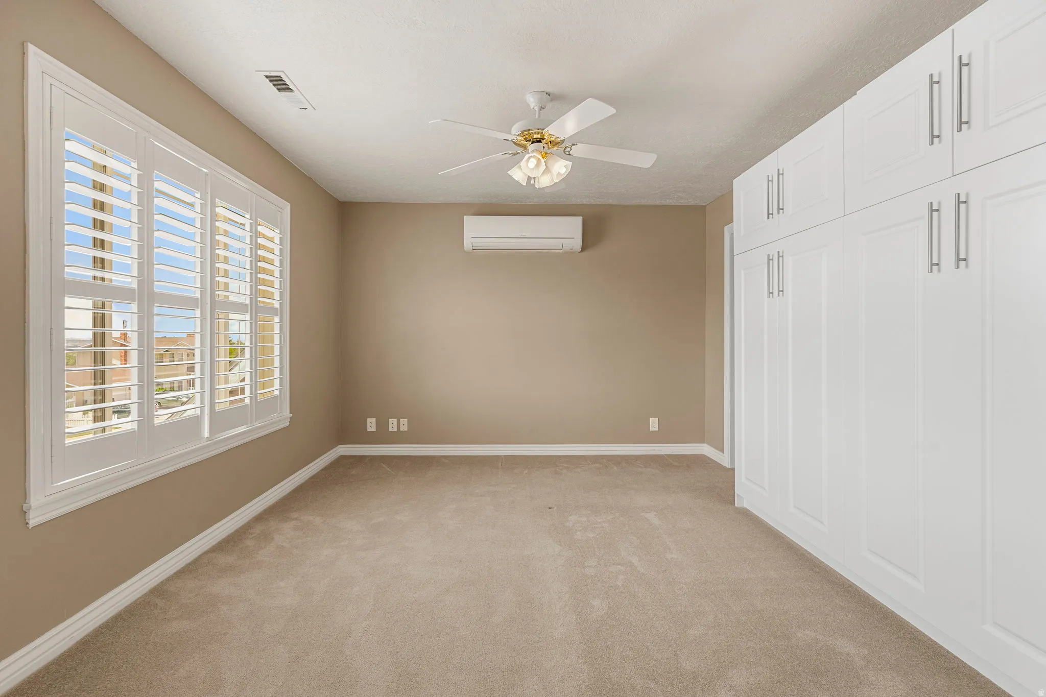 Expansive room featuring built-in white paneled cabinetry, a ceiling fan, and large windows with white plantation shutters