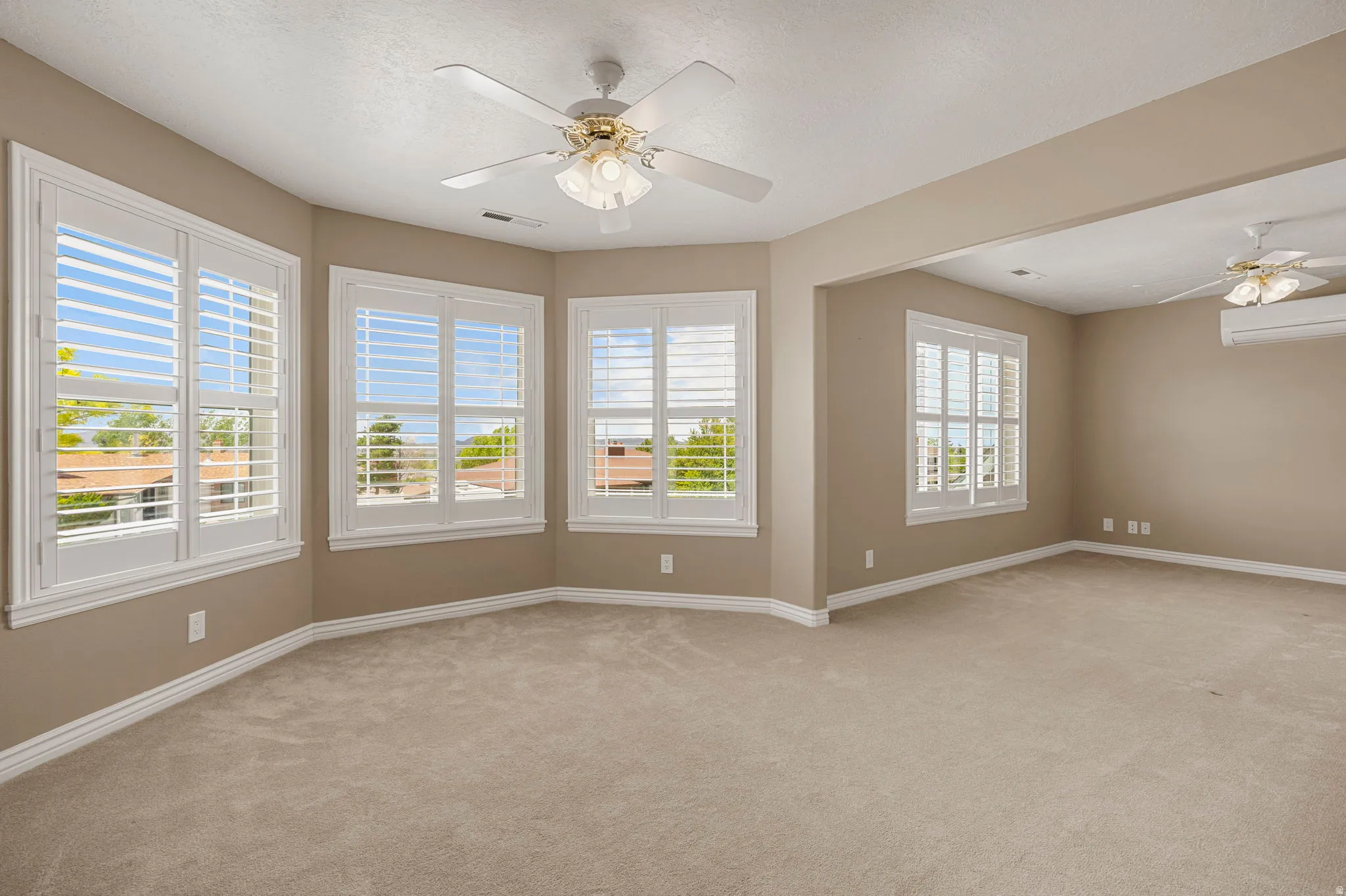 Expansive room featuring multiple windows with plantation shutters, soft carpet flooring, and neutral wall tones