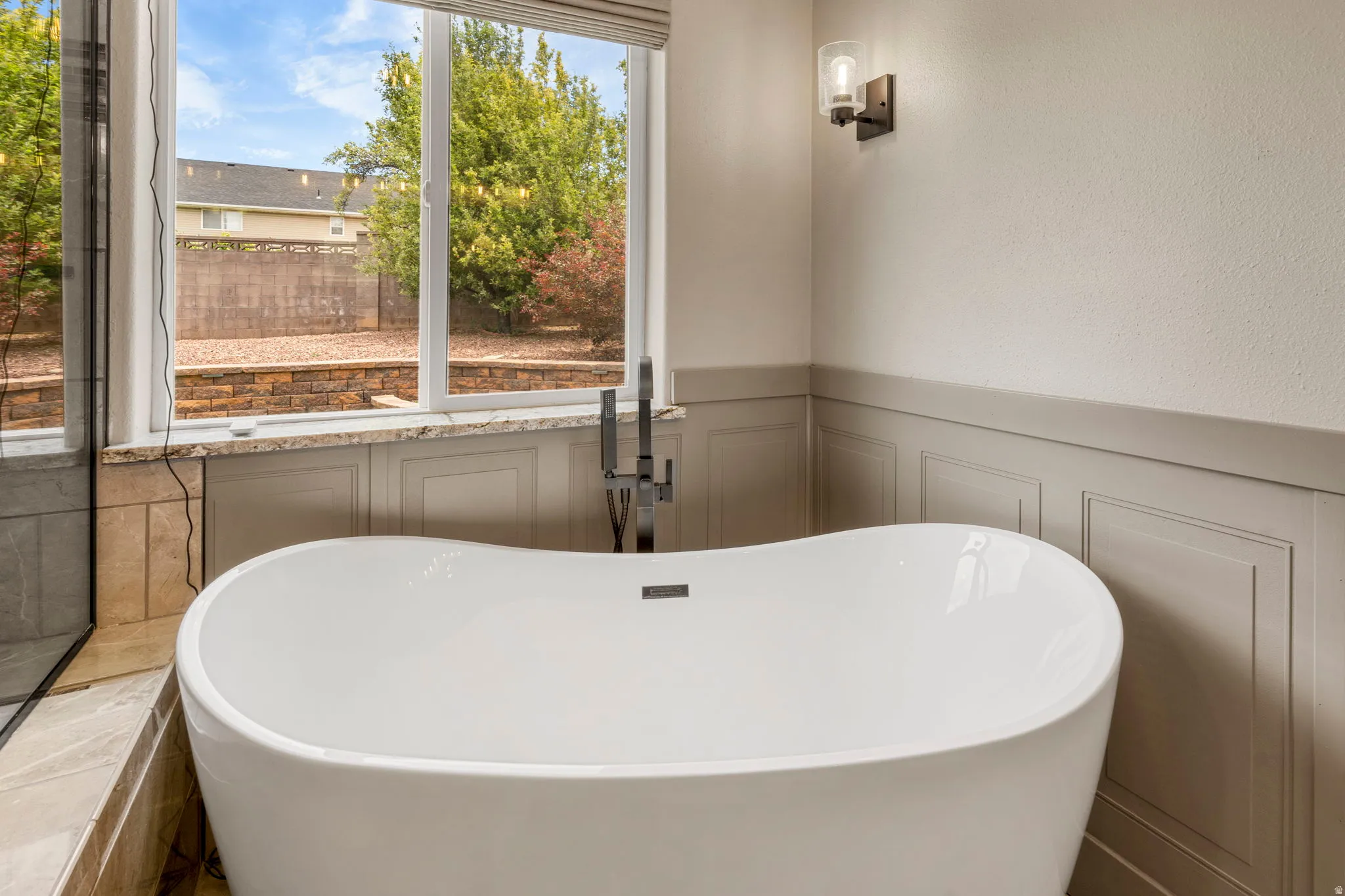 Freestanding bathtub with a floor-mounted fixture, complemented by wainscoting and a sconce light fixture