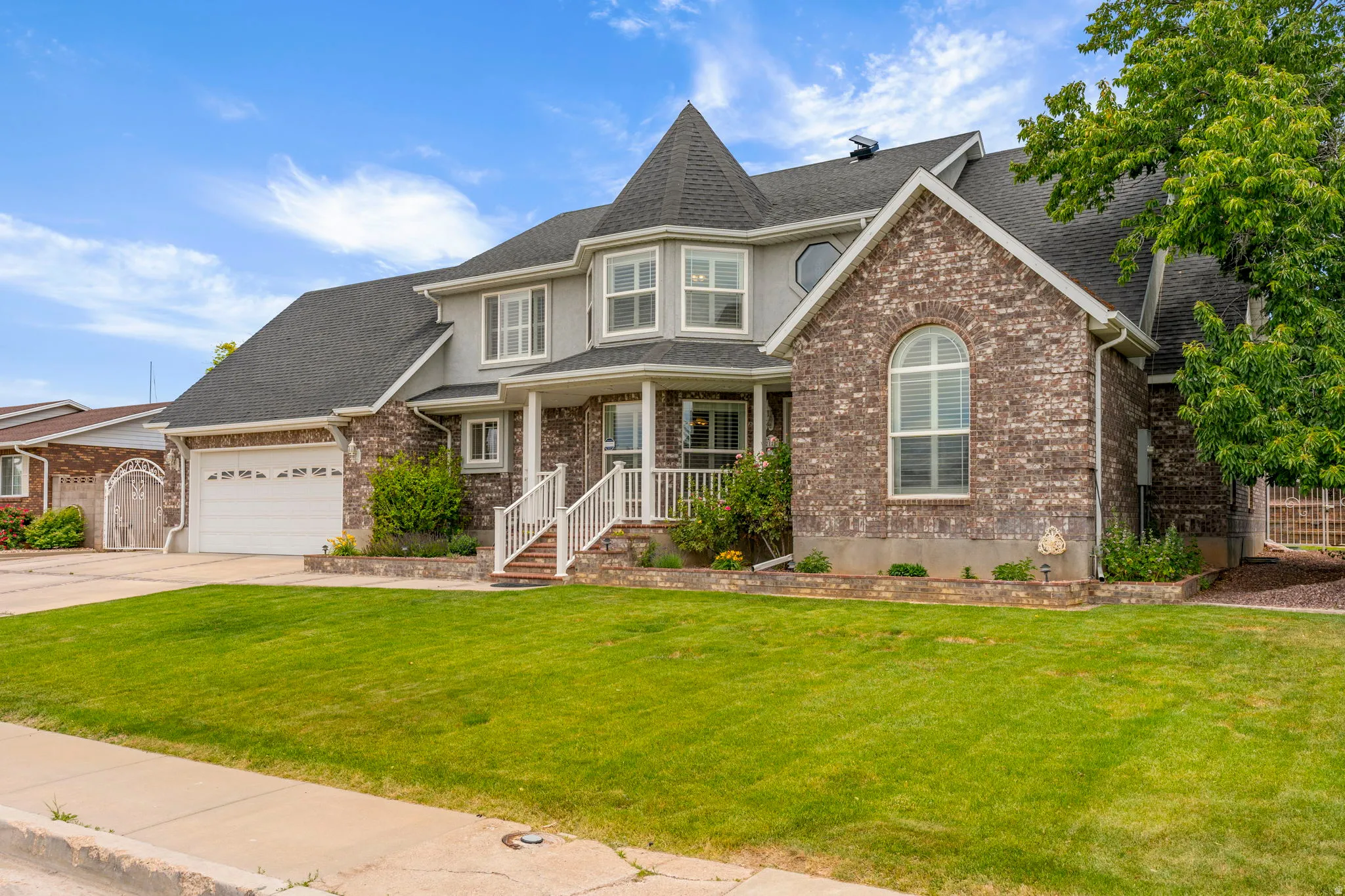 Brick and stucco exterior with a prominent turret, a covered front porch, a two-car garage, mature landscaping, and an arched window accent