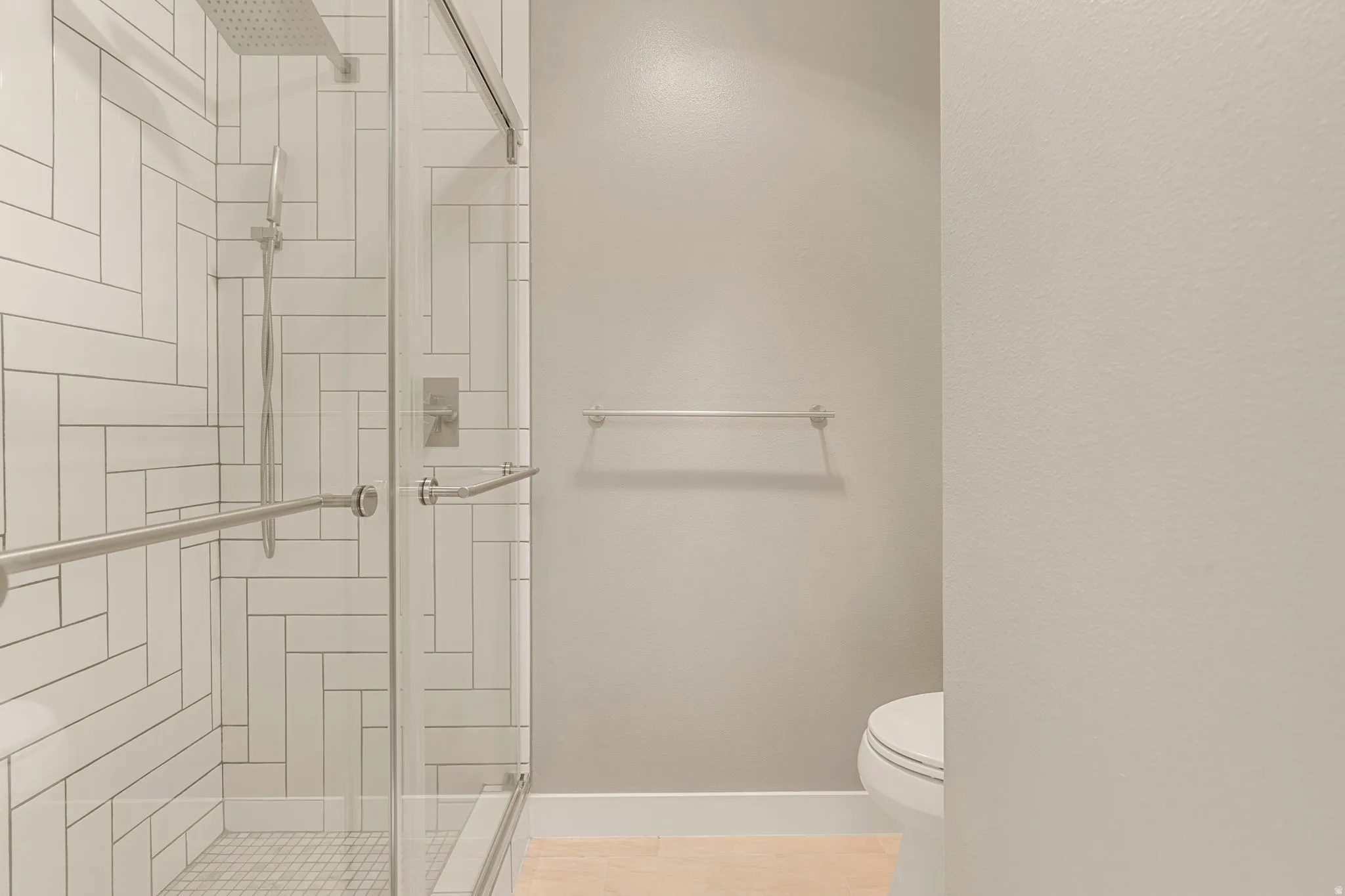 Shower enclosure with clear glass door, featuring white subway tile in a herringbone pattern and a rain shower head