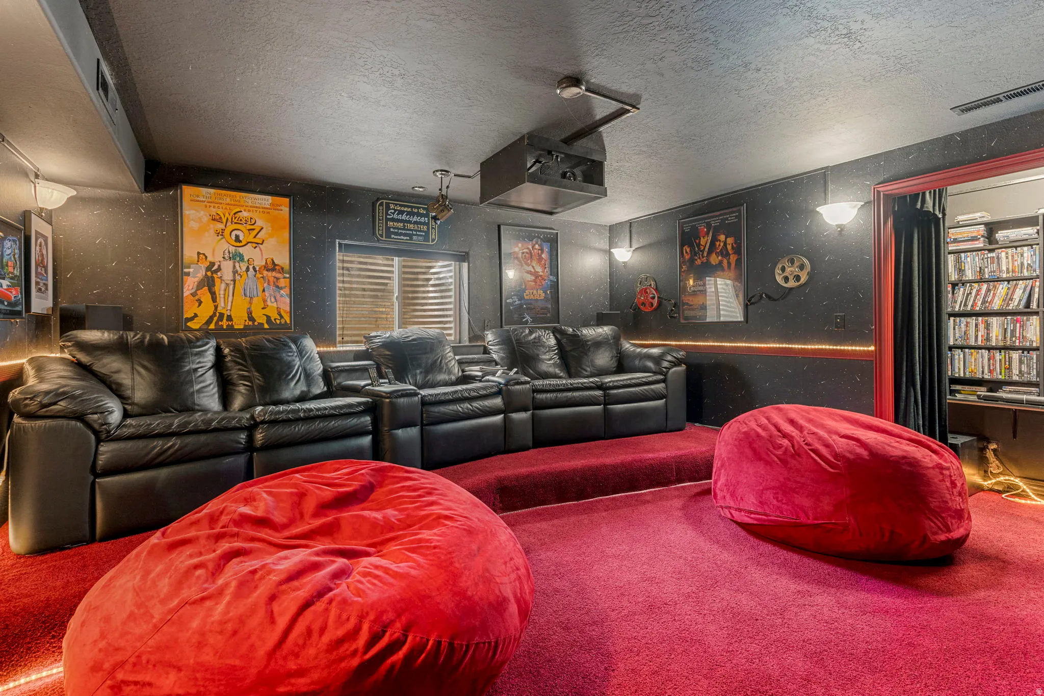Dedicated media room featuring tiered seating, red carpeting, a ceiling-mounted projector, and wall-mounted sconces