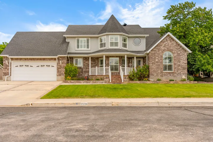 Two-story residence featuring a brick and siding facade, covered front porch, integrated two-car garage, and mature landscaping