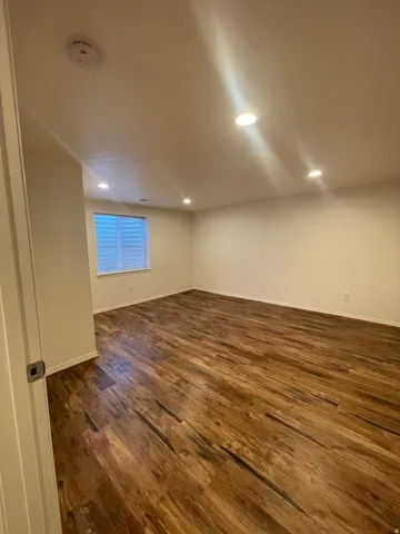 Spacious room featuring wood-finish flooring, recessed lighting, and a window with horizontal blinds