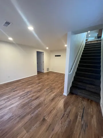 Wood-finish flooring throughout, recessed lighting, white trim, and a carpeted staircase with white railings