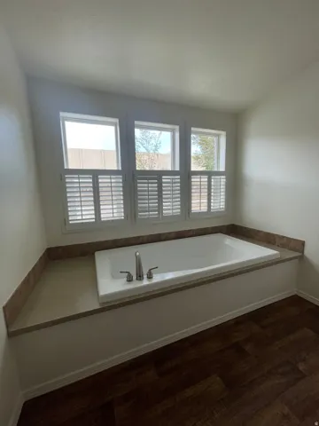 Built-in soaking tub with deck-mounted fixtures, surrounded by a stone-finish countertop and backsplash