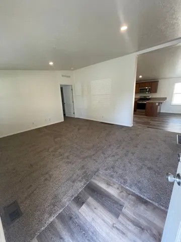 Recessed lighting, wood-finish flooring, carpeted area, white walls, and a partial kitchen with wood cabinetry