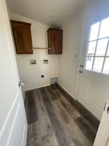 Laundry area featuring wood-finish flooring, white walls, and built-in wood cabinetry
