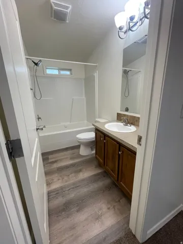 Bathroom featuring wood-finish flooring, a vanity with wood cabinetry, a built-in tub with a shower, and a recessed window