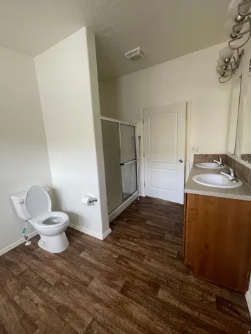 Dual vanity with undermount sinks, wood-finish flooring, and a glass-enclosed shower