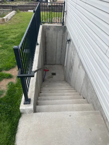 Exterior basement entry featuring concrete stairs and black metal railings