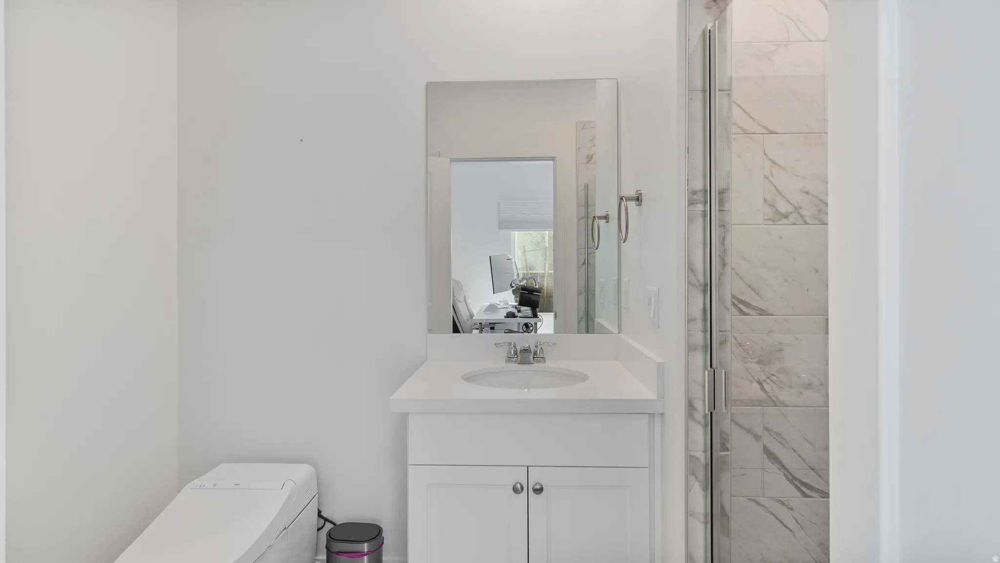 White vanity with a single basin sink and a chrome faucet, illuminated by a rectangular mirror