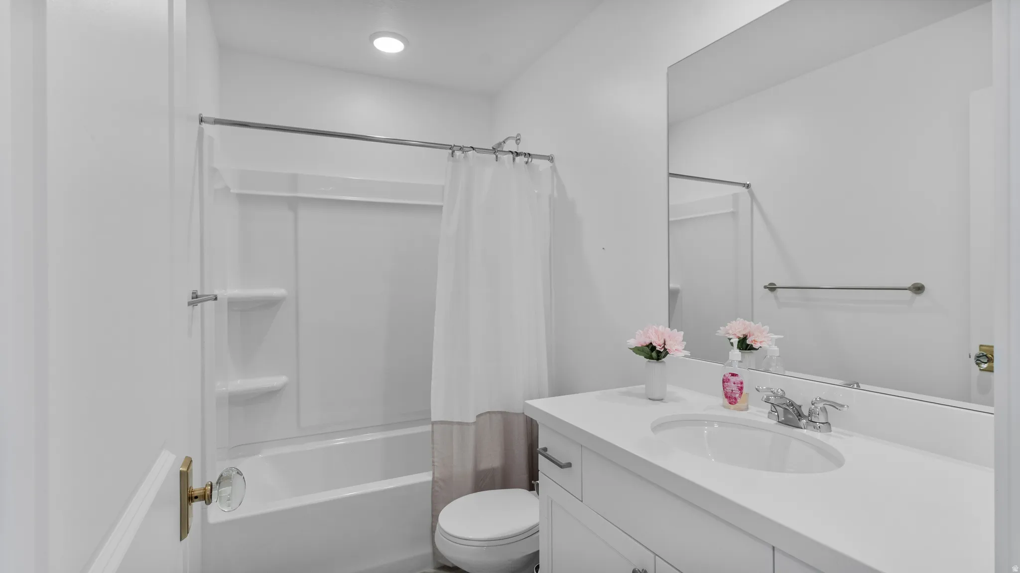 Bathroom featuring a white bathtub with an integrated shower, a white vanity with an integrated sink, a large wall-mounted mirror, and recessed lighting
