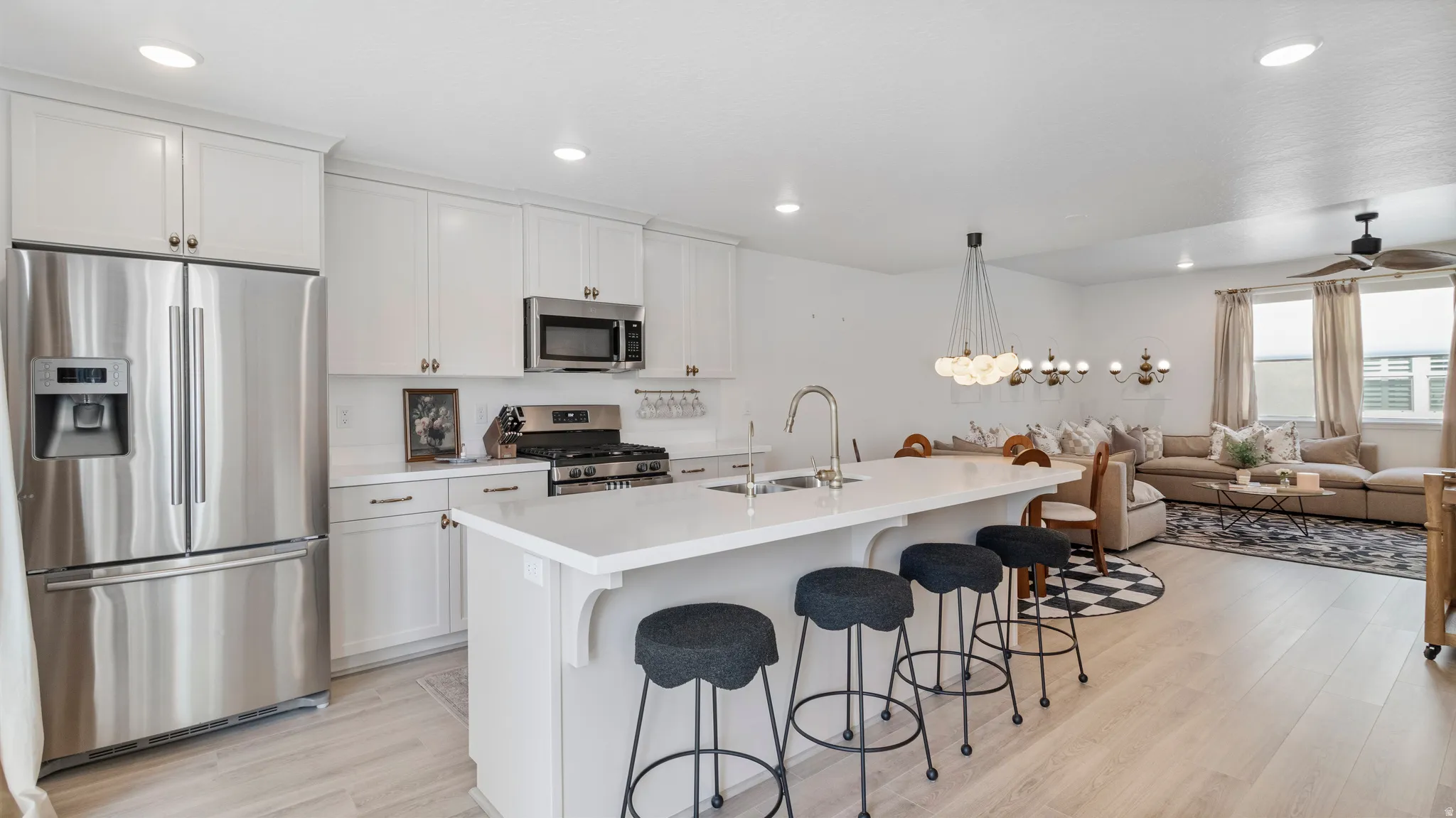 Open-concept kitchen featuring white shaker cabinetry, stainless steel appliances, a center island with sink and seating, and light wood-finish flooring