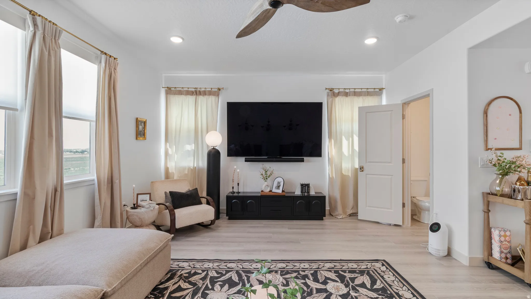 Spacious living area featuring light wood-finish flooring, recessed lighting, a ceiling fan, multiple windows with roller shades, and a panel door