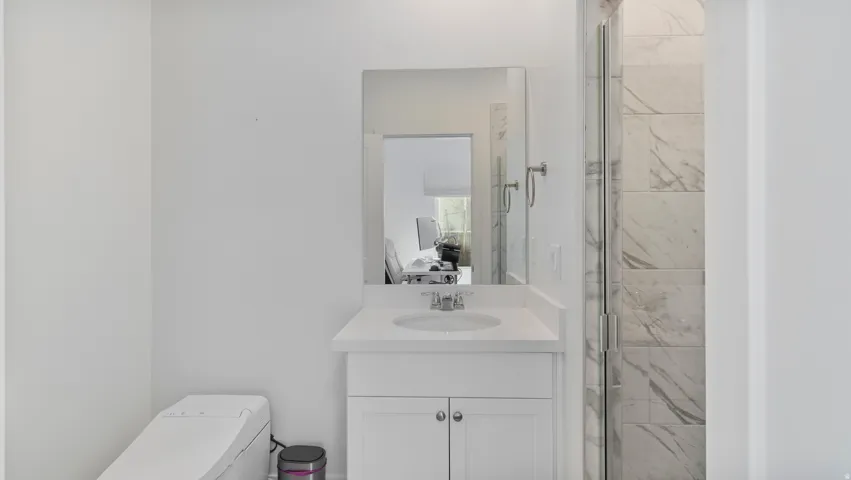 White vanity with a single basin sink and a chrome faucet, illuminated by a rectangular mirror