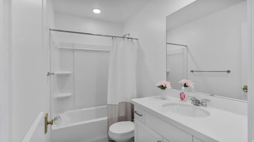 Bathroom featuring a white bathtub with an integrated shower, a white vanity with an integrated sink, a large wall-mounted mirror, and recessed lighting