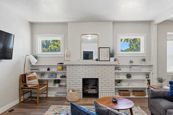 Living area featuring a white brick fireplace with hearth, integrated shelving, and wood-finish flooring