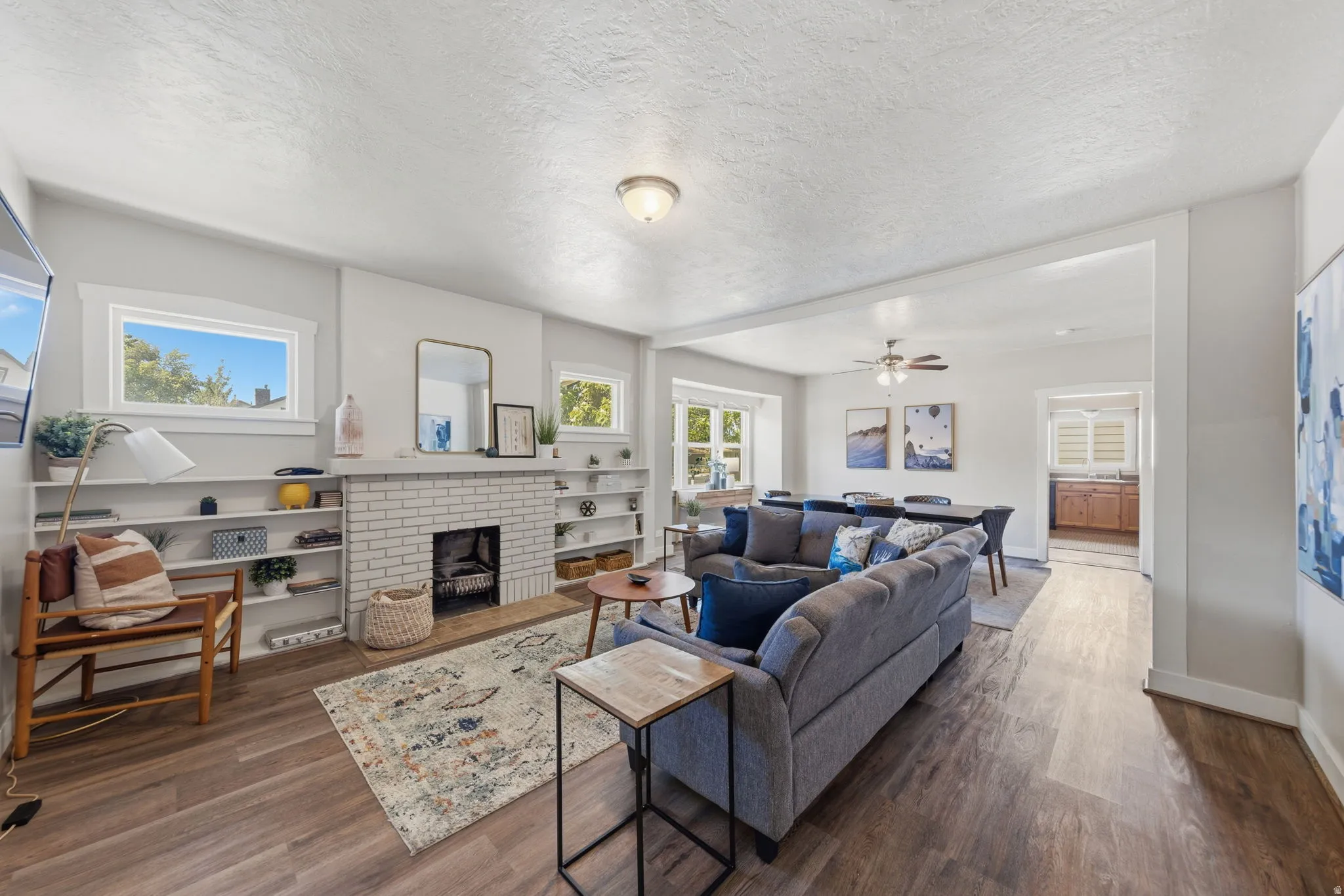Spacious living area featuring wood-finish flooring, a white brick fireplace with a hearth, and built-in shelving flanking the fireplace