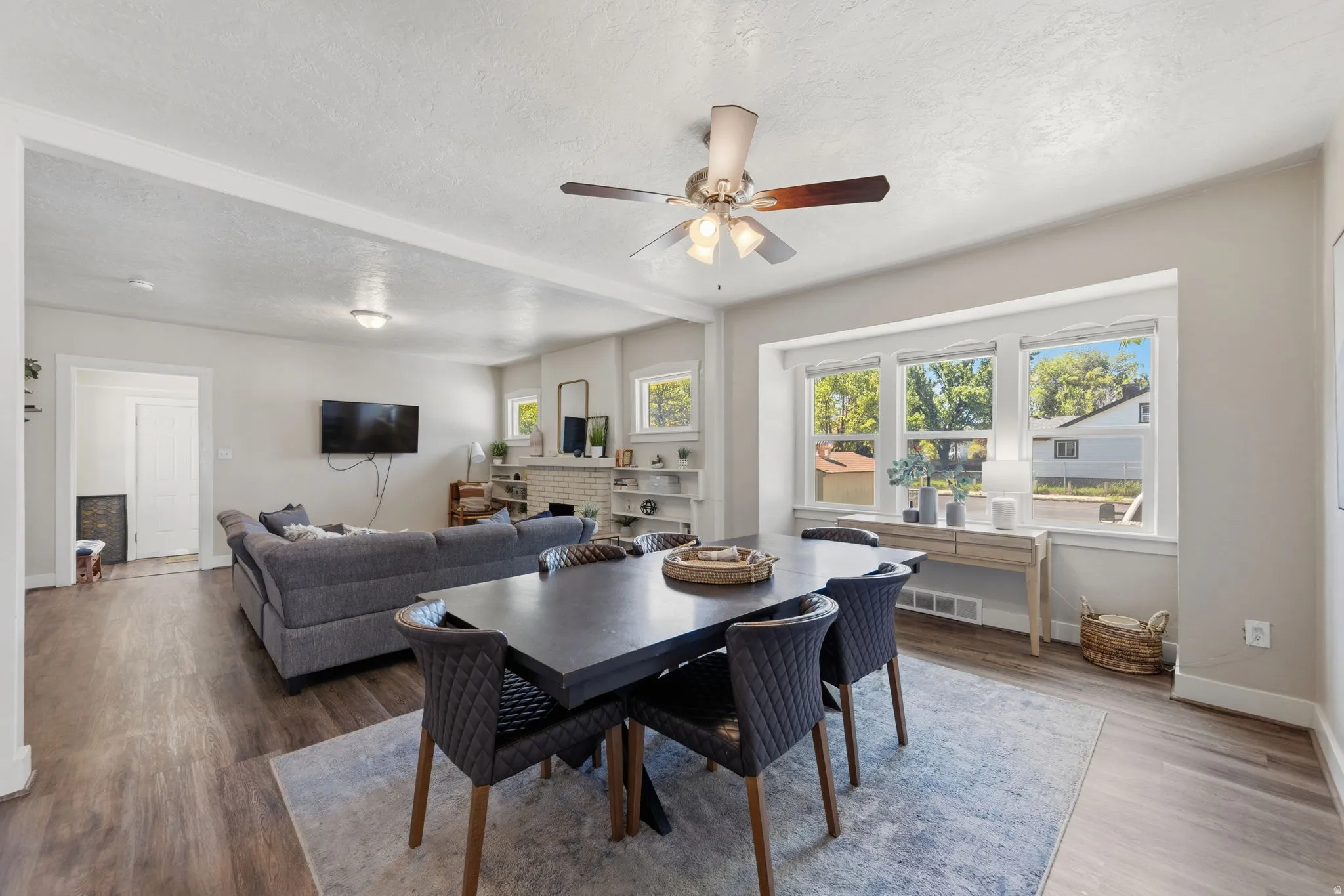 Open-concept living space featuring wood-finish flooring, a contemporary ceiling fan, and a wide bay window