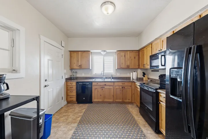 Kitchen featuring natural wood cabinetry, dark countertops, and black appliances
