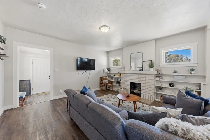 Living area featuring wood-finish flooring, a white brick fireplace, built-in shelving, and light gray walls