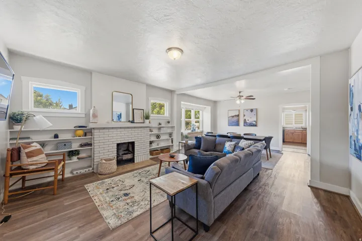 Spacious living area featuring wood-finish flooring, a white brick fireplace with a hearth, and built-in shelving flanking the fireplace