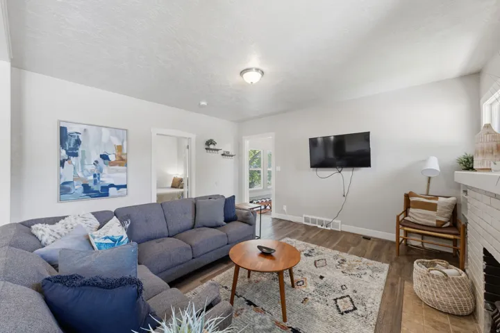 Living area featuring wood-finish flooring, light grey wall paint, a white brick fireplace, and a white mantel