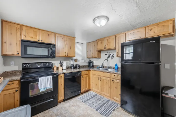 Kitchen featuring extensive wood cabinetry, black appliances, textured countertops, and a double basin sink