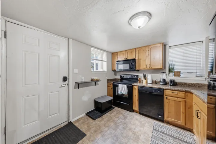 Kitchen featuring light wood cabinetry, stone-finish countertops, and black appliances
