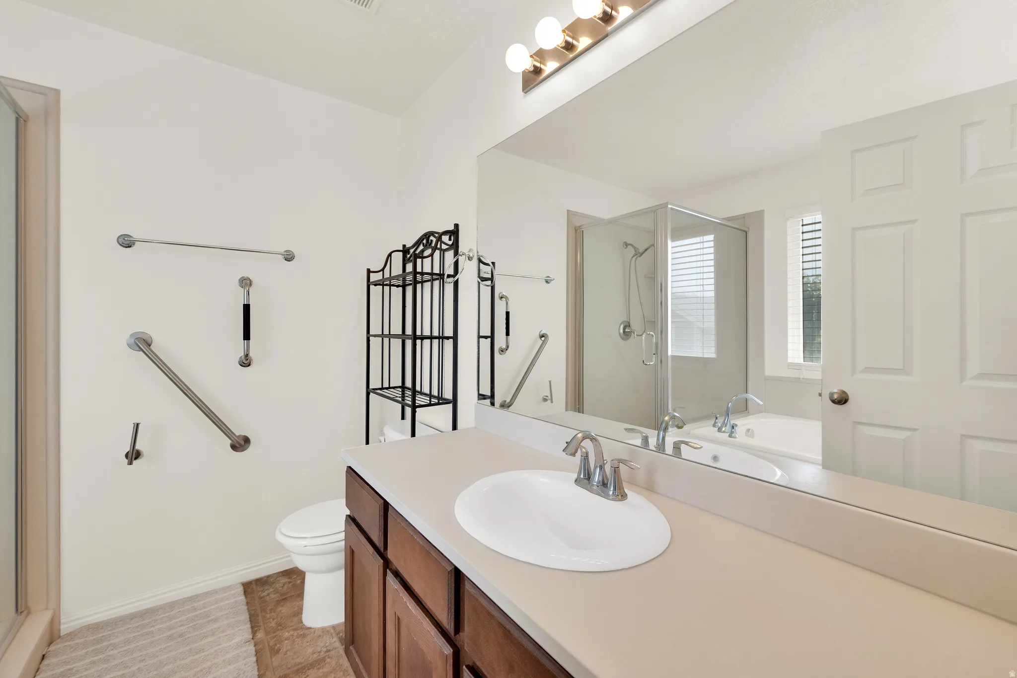 Bathroom featuring a single vanity with a white oval sink and chrome faucet, a large wall-mounted mirror, a glass-enclosed shower, and a separate soaking tub