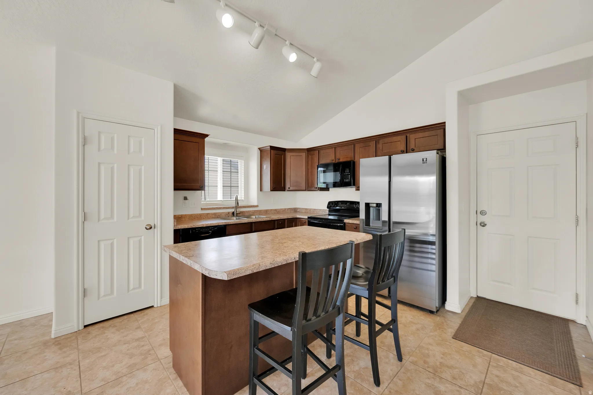 Kitchen featuring a central island with counter seating, rich wood cabinetry, stainless steel refrigerator, black range, and ample counter space
