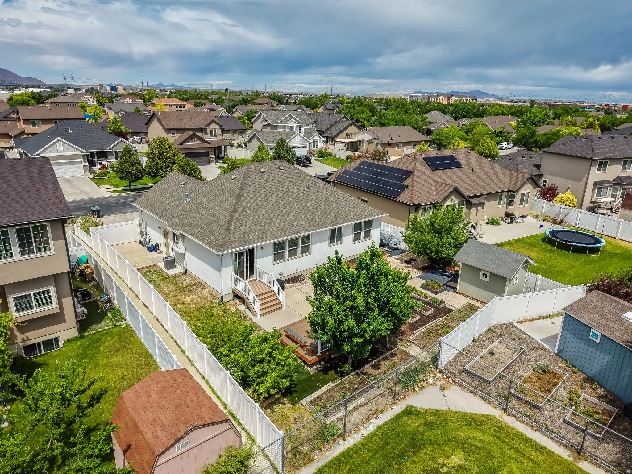 Rear exterior featuring a white vinyl fence, multi-level deck, garden beds, and mature landscaping