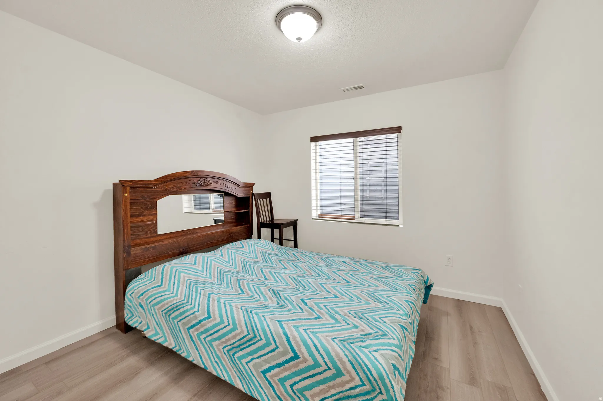 Bedroom featuring wood-finish flooring, white walls, and a window with blinds